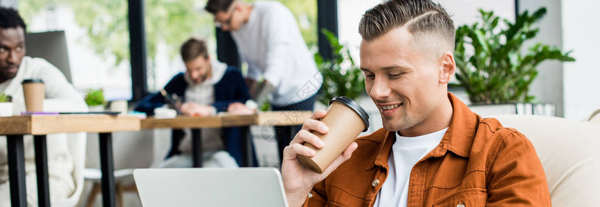 年轻商人在多元文化同事附近的办公室工作时喝咖啡去和使用笔记本电图片
