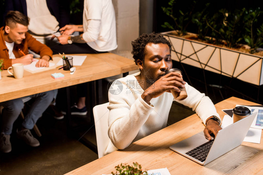 年累的非洲商人在同事附近的办公室里晚上坐在工作场合时喝咖啡去上班图片