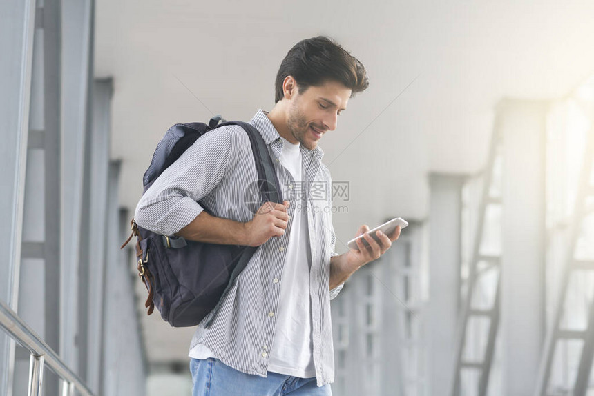 航站楼内的Wifi带背包的男子旅行者在机场使用智能手机浏览互联网或在线图片