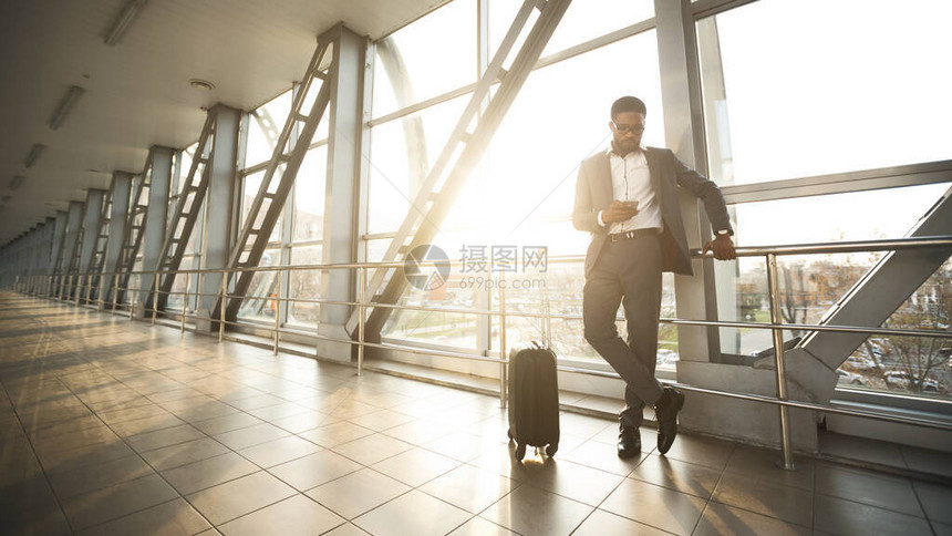 黑人企业家利用移动电话在机场航站楼等待飞行的旅行衣物图片