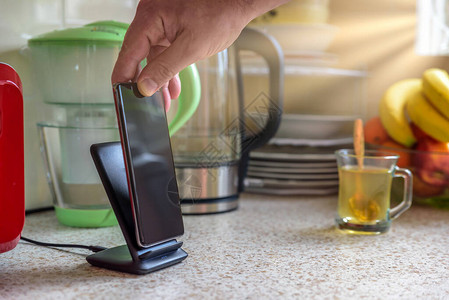 智能手机在厨房桌面上的充电座上进行无线充电男手图片