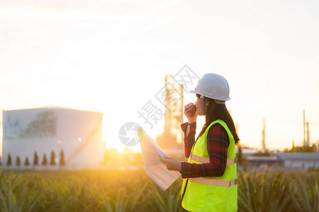 亚洲女技术员工业程师使用对讲机和手持蓝图在炼油厂工作图片