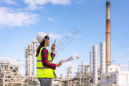 亚洲女技术员工业程师使用对讲机和手持蓝图在炼油厂工作图片