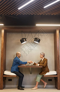 商务会议期间两人坐在室内咖啡厅桌边握手的侧视全长肖图片