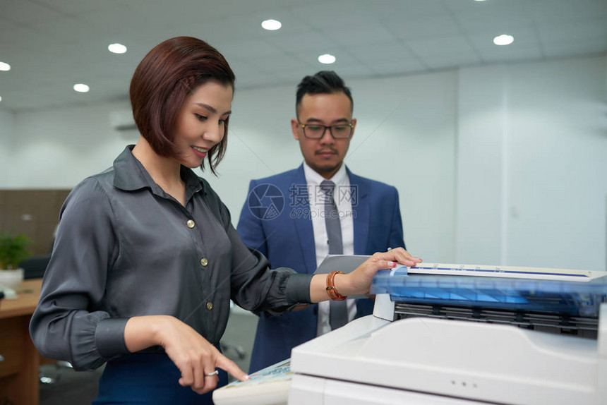 微笑的亚洲秘书在复印机上复制图片