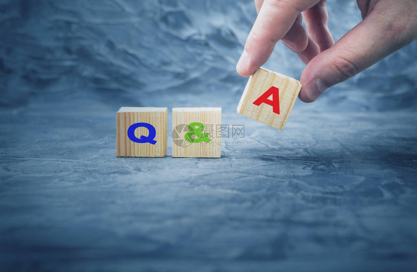 手把带有字母QA的木块立方体放在木桌上问答图片