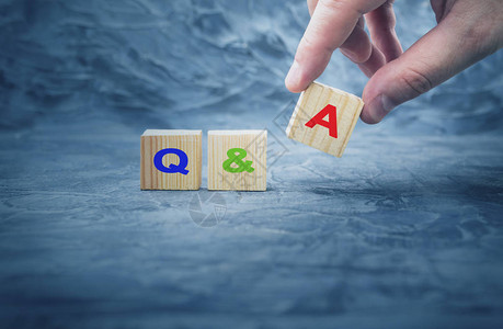 手把带有字母QA的木块立方体放在木桌上问答背景图片