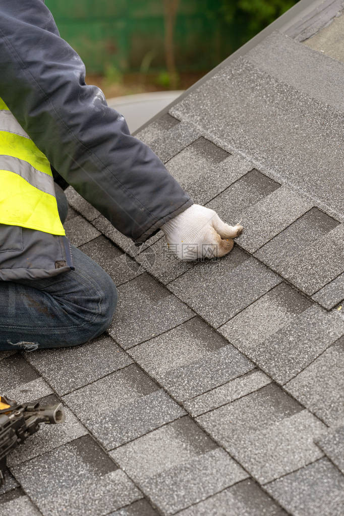 在建房屋顶上安装沥青或沥青瓦的特殊防护工作服和发光专业屋顶工人的垂图片