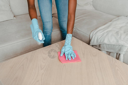 非洲裔美国妇女戴着橡胶手套在客厅用清洁剂和抹布清洁图片