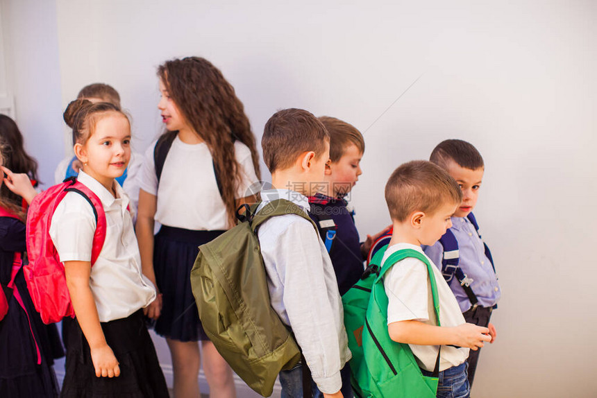 一群快乐的小学生在学校学校走廊里穿着制服背图片