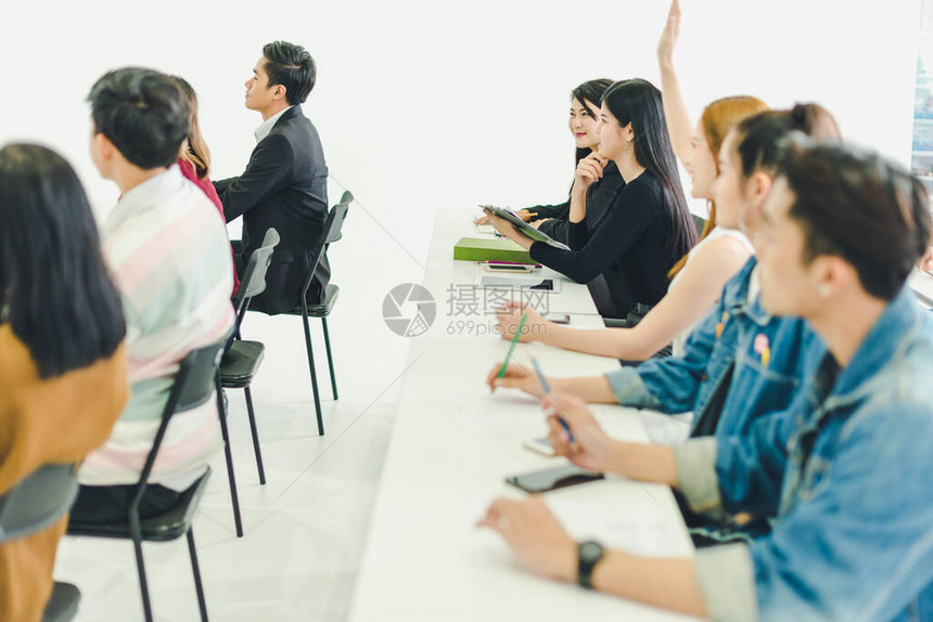 亚洲人参加研讨会并在培训室聆听演讲者的演讲有些人会记笔有人举手询问解说员并在演讲图片
