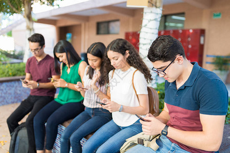 一群坐在大学校园里的朋友在用智能手机图片