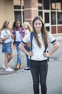 可爱的西班牙裔青春期前青少年学生放学后和朋友一起出去玩有选择地关注站在校舍外背景图片