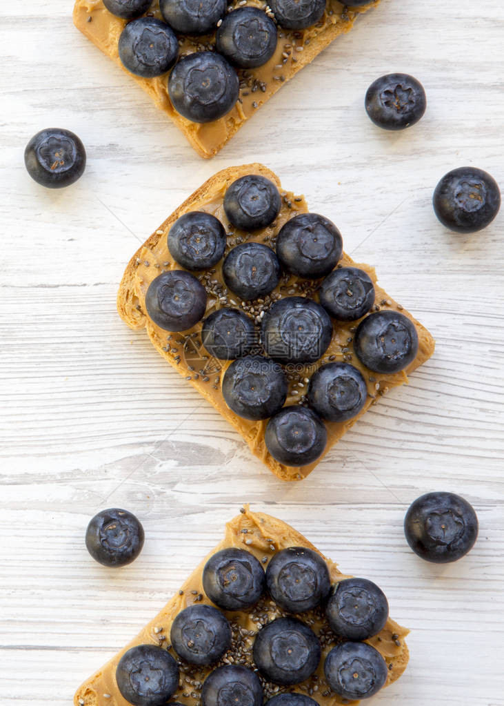 用花生酱蓝莓和辣椒种子在白色木质表面的Vegan烤面包图片