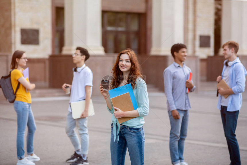 快乐的女学生在休息时喝咖啡站在大学楼外图片