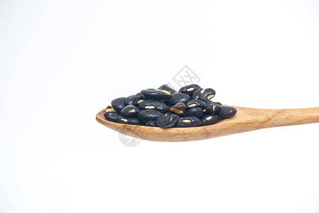 在白色背景上隔离的木勺中的黑豆粒图片