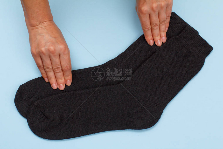 女手与一对黑温暖的羊毛男袜子在蓝色背图片