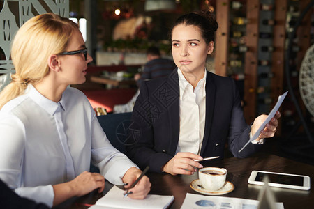 两位优雅的年轻女员工坐在咖啡馆里讨论文图片