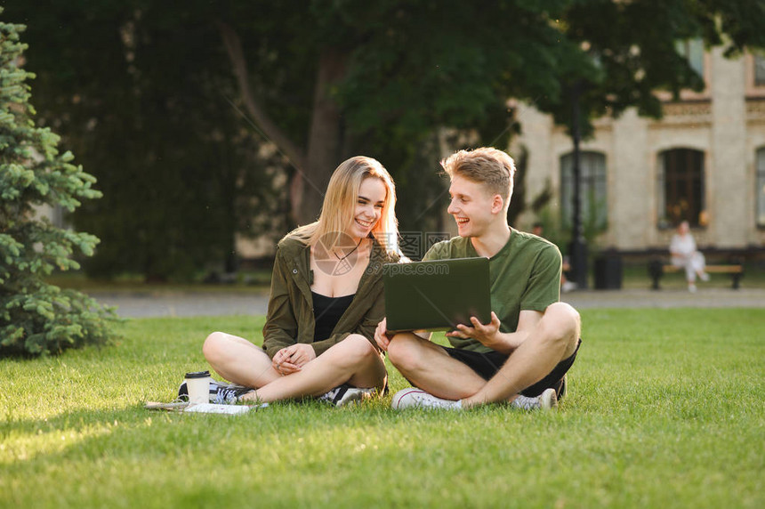 快乐的大学生在校园草坪上使用笔记本电脑交流交谈图片