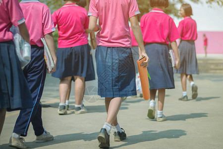 穿着粉红色衬衫和蓝裙子的小学女生与朋友一起步行到教室去图片