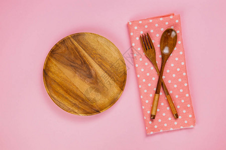 粉红色背景上带勺子叉子和粉红色圆点布餐巾的木盘图片