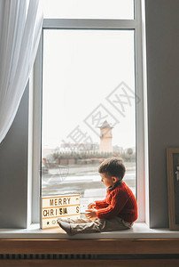 穿着温暖毛衣的小男孩坐在窗边背景图片