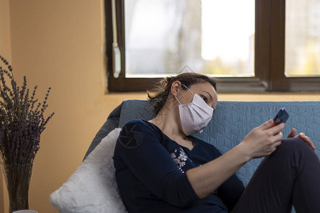 戴医疗面具坐在沙发上看智能手机的抑郁妇女图片