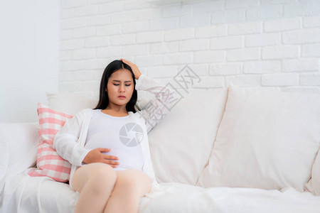 年轻孕妇头痛坐在家里客厅的沙发上怀孕症状期望父母身份概图片