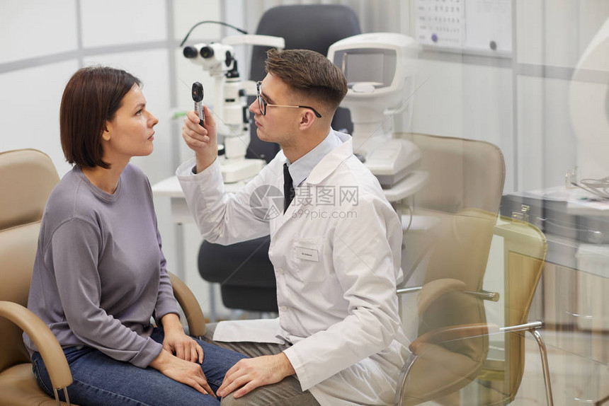 在眼科诊所复制空间咨询期间检查女病人视力的年轻观察家的侧面照片图片
