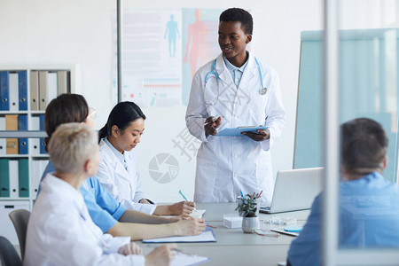 年轻非洲裔美国医生在医学委员会或诊所会议期间站在桌边发表演讲的肖图片