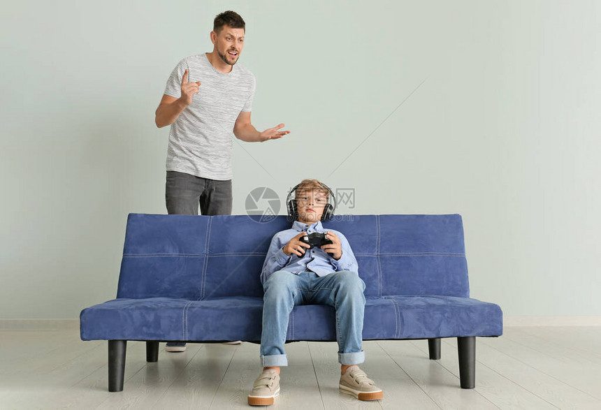小男孩玩电子游戏忽视他愤怒的父亲在图片