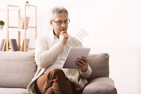 退休男子在数字平板电脑上看新闻坐图片