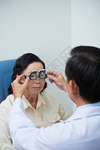 眼科医生帮助老年病人在检查其视力时戴可调适图片
