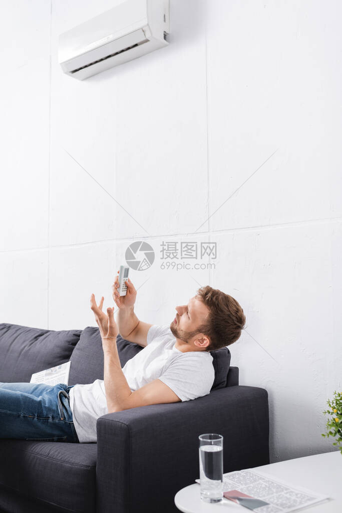 混淆的男子试图在家中用遥控制器开通空调图片