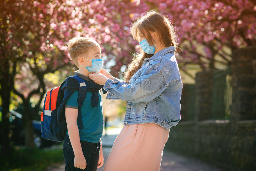 小学生准备上学母亲在儿子脸上戴安全面具在户外背着包的可爱男孩回到学校的概念用于预防冠状的医用口罩图片