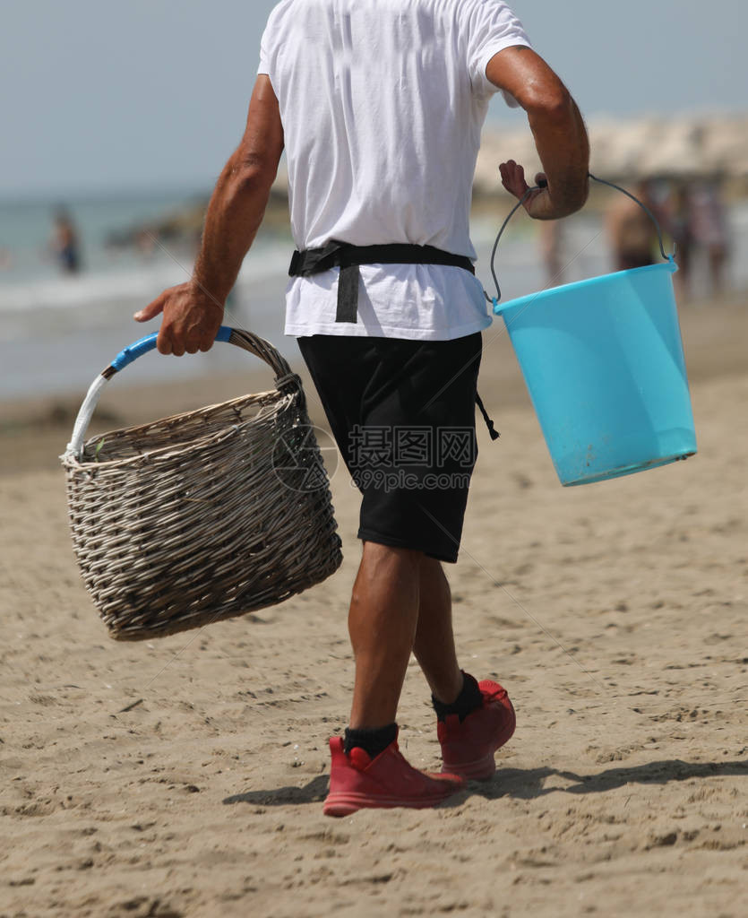 小贩在沙滩上提了一个木娄和一个水桶图片