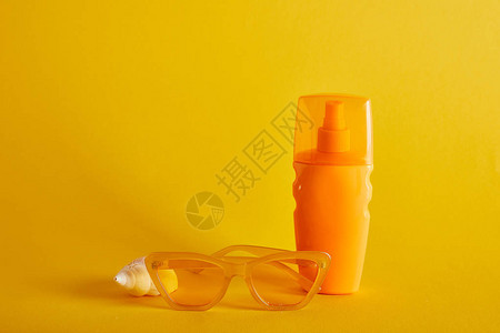 在太阳镜附近的橙色瓶子和深黄色背景的贝壳上图片