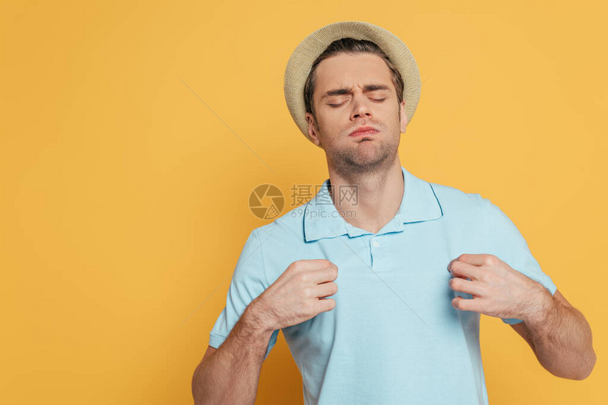 闭着眼睛的男子因热和触摸被黄色孤立的T恤衫图片