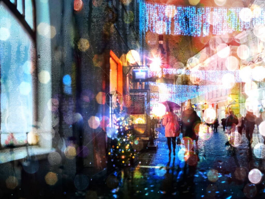 城市模糊的光夜在下雨的圣诞假期街道装饰人们在雨伞下图片