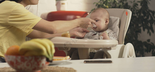 一名年轻母亲在厨房用婴儿食物喂孩图片
