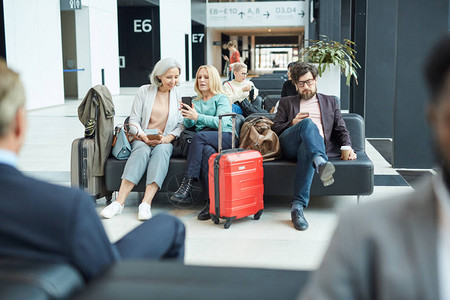 一群人在离港休息室聊天和在智能手机互联网上冲浪时等待航班的横向水平图片