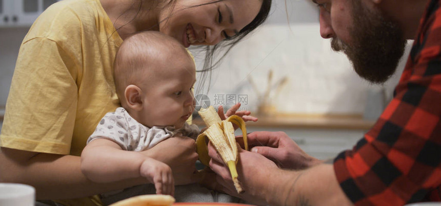 一对快乐的年轻夫妇在厨房用香蕉喂婴儿时图片