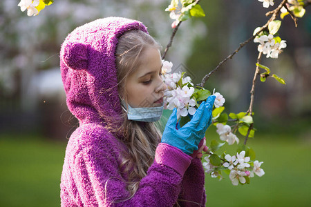 可爱的女孩在开花的苹果树上戴着医用面罩和乳胶防护手套图片