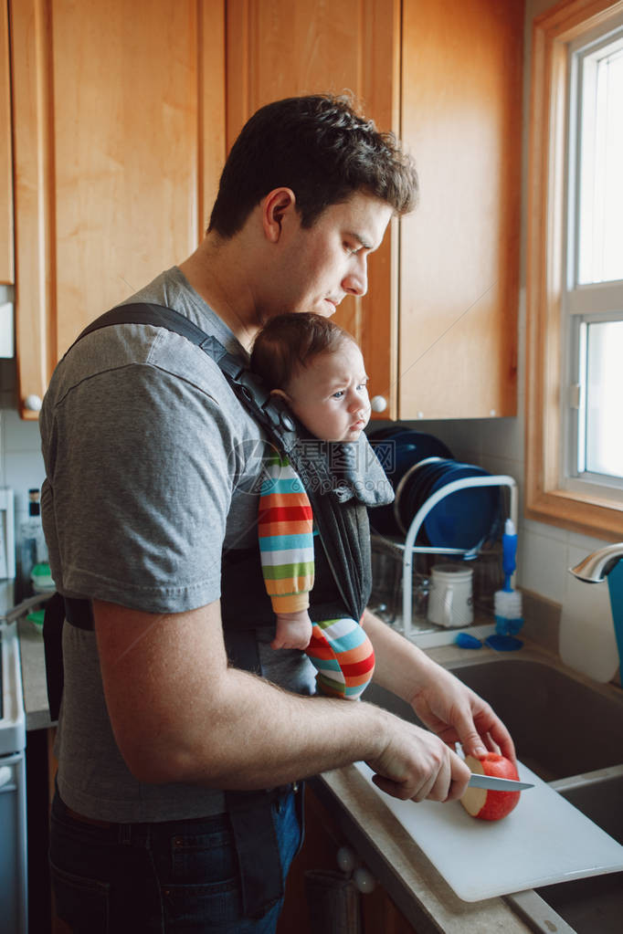 年轻的白种人父亲带着刚出生的婴儿在准备午餐的载体中男人父母带着孩子站在厨房里做食物真实的生活方式坦诚真实的时刻单身爸图片