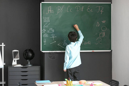 可爱的小男生在教室的黑板上写字图片