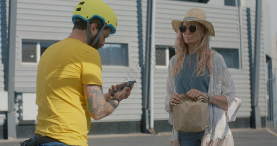 中度自行车送信员向站在街上和电话聊天的妇女提供食物背景图片