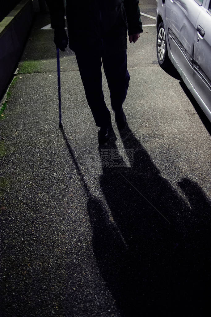 用蓝色伸缩铝杖保持平衡的手杖夜间在法国街上行走的老人剪影的低高度医图片