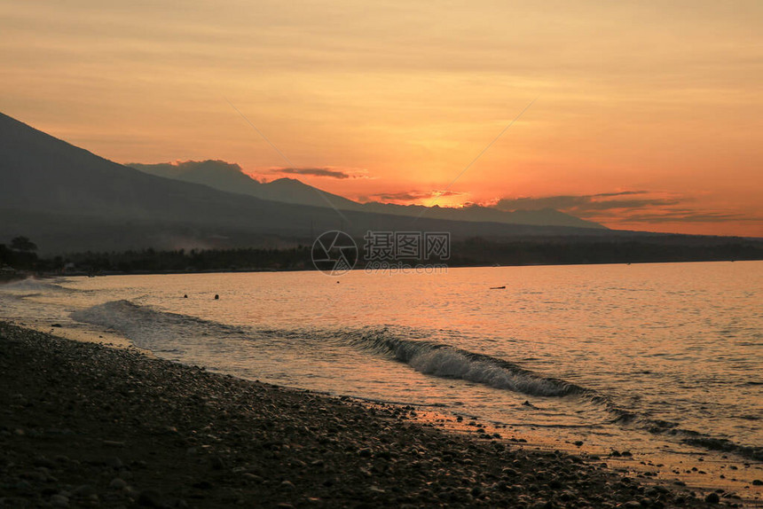 热带岛屿的橙色日落太阳落日照亮的平静海火山和脉全景渔船在海滩上停靠图片