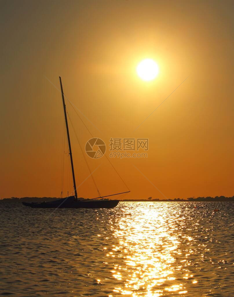 日落时停泊在海上的帆船和背景中的岬角图片