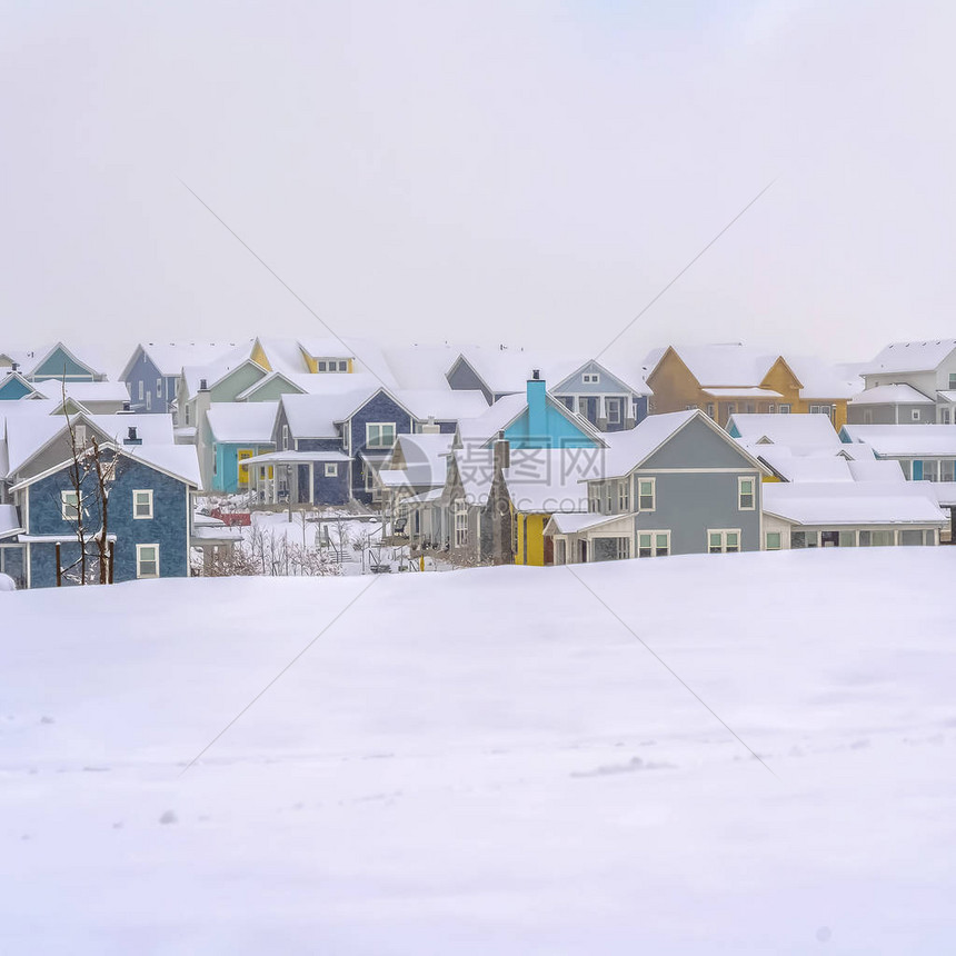 方形框架与五颜六色的房子的冬天风景反对多云天空背景前景中可以看到被新雪覆图片